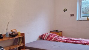 Una habitación pequeña y acogedora con una cama individual, una mesa de madera, una silla morada y un ventanal con vistas a árboles.