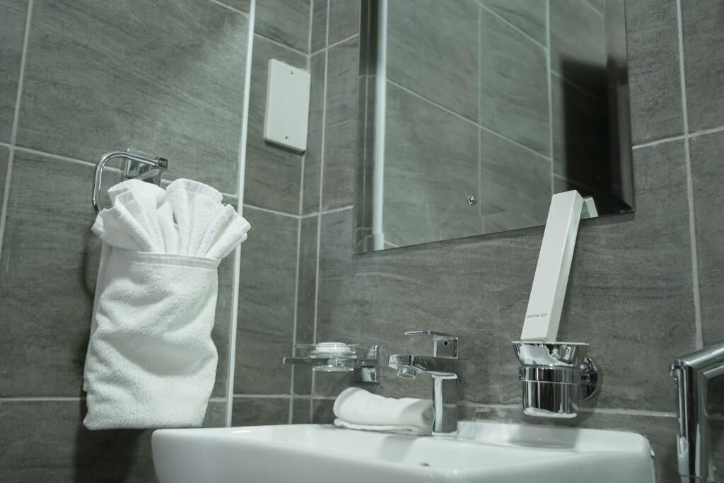 Une salle de bain avec un lavabo blanc, des robinetteries chromées et un porte-serviettes avec des serviettes pliées.