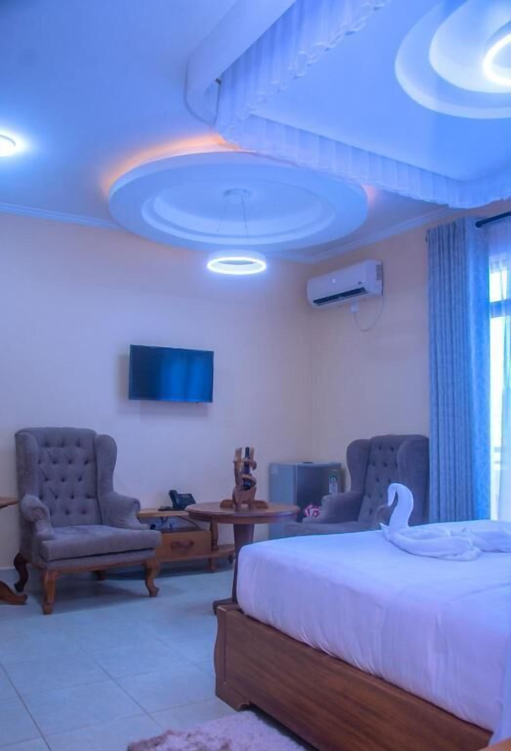 A hotel room with a bed, two armchairs, a TV, and a ceiling with circular light fixtures.