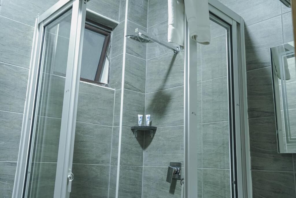 Ducha en esquina con mampara de vidrio, una ventana pequeña y estante con artículos de tocador.