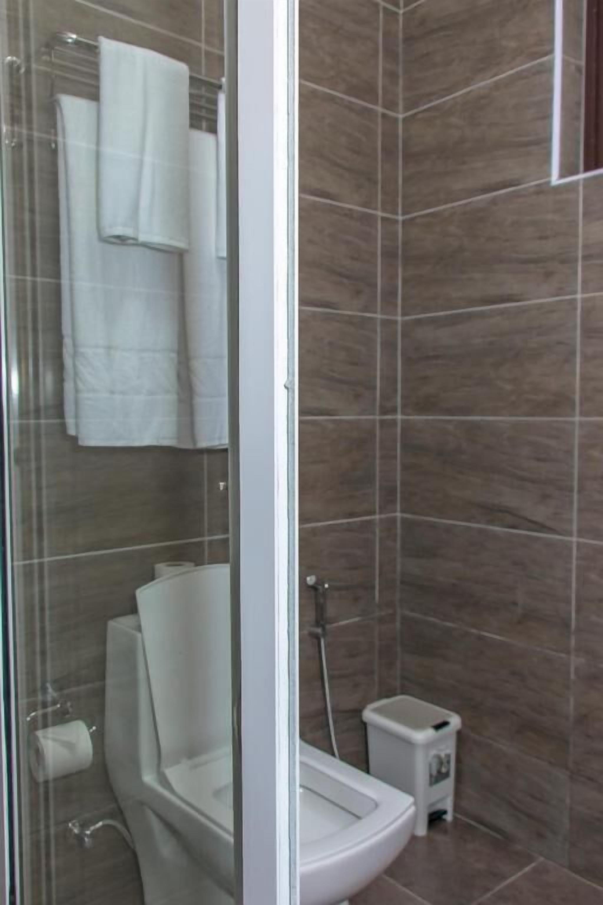 A modern bathroom with a glass shower enclosure, a toilet, and a small trash bin.