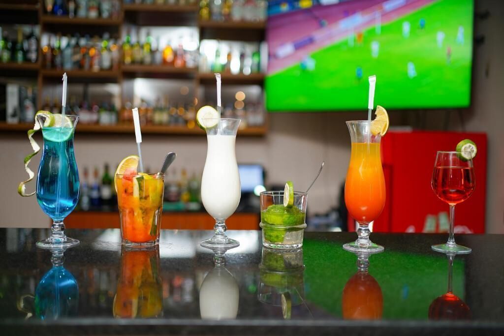 A bar with various colorful drinks, a television in the background, and shelves with bottles.