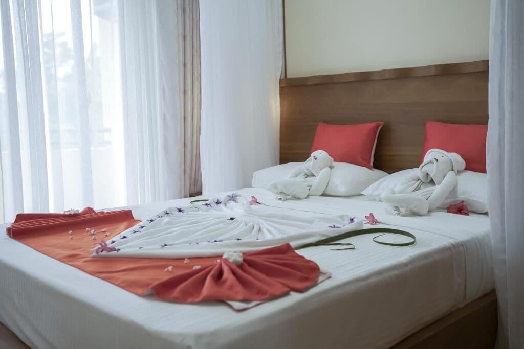 Une chambre d’hôtel avec un lit bien fait, du linge de lit blanc et des oreillers rouges.
