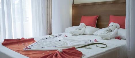 A hotel room with a neatly made bed, white linens, and red pillows.
