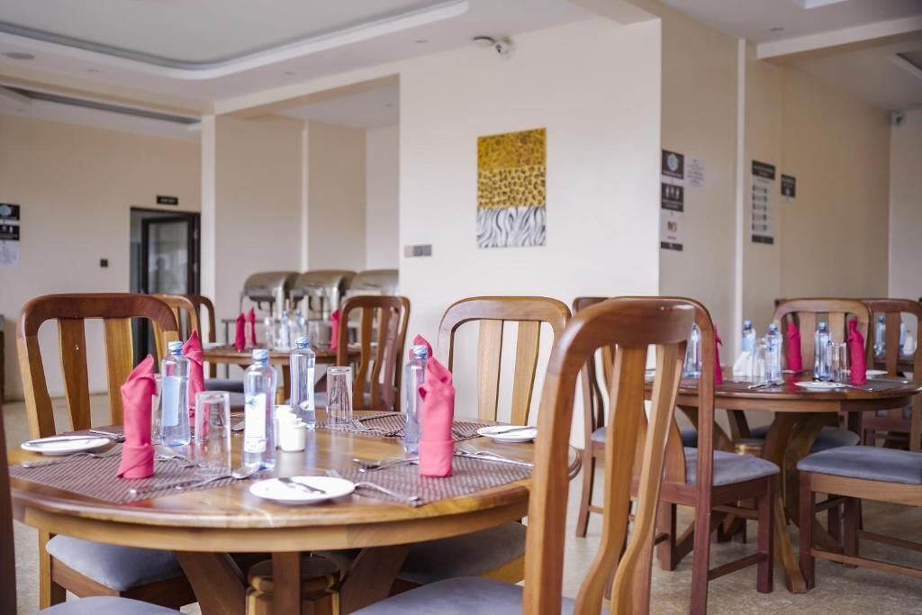 A dining area with round wooden tables set for four, each with pink napkins, clear glasses, and cutlery.