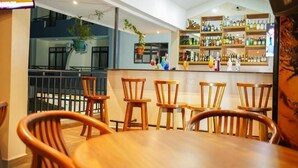 Zona de bar con sillas y mesas de madera, estantes con botellas y vistas al exterior.