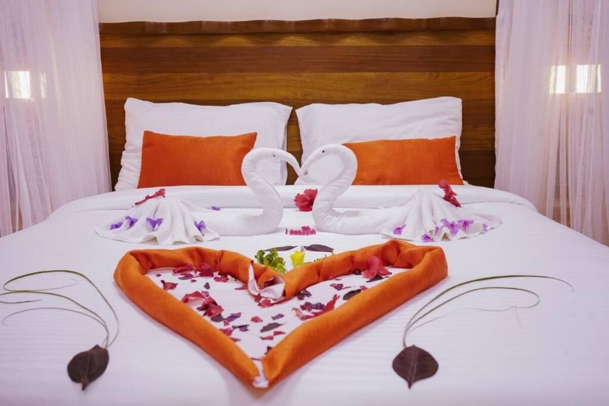A neatly made bed with white linens, orange pillows, and a decorative arrangement of towels and flowers.