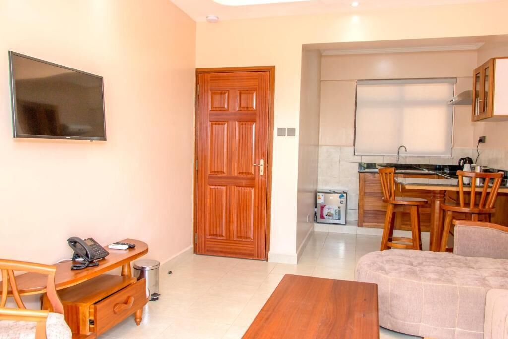 A compact living space with a wooden desk, a sofa, a TV, and a kitchen area with a dining set.