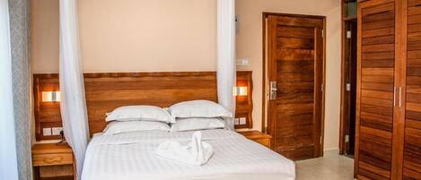 Una cama bien tendida con un almohadón con forma de cisne blanco, cabecero de madera y lámparas de noche.