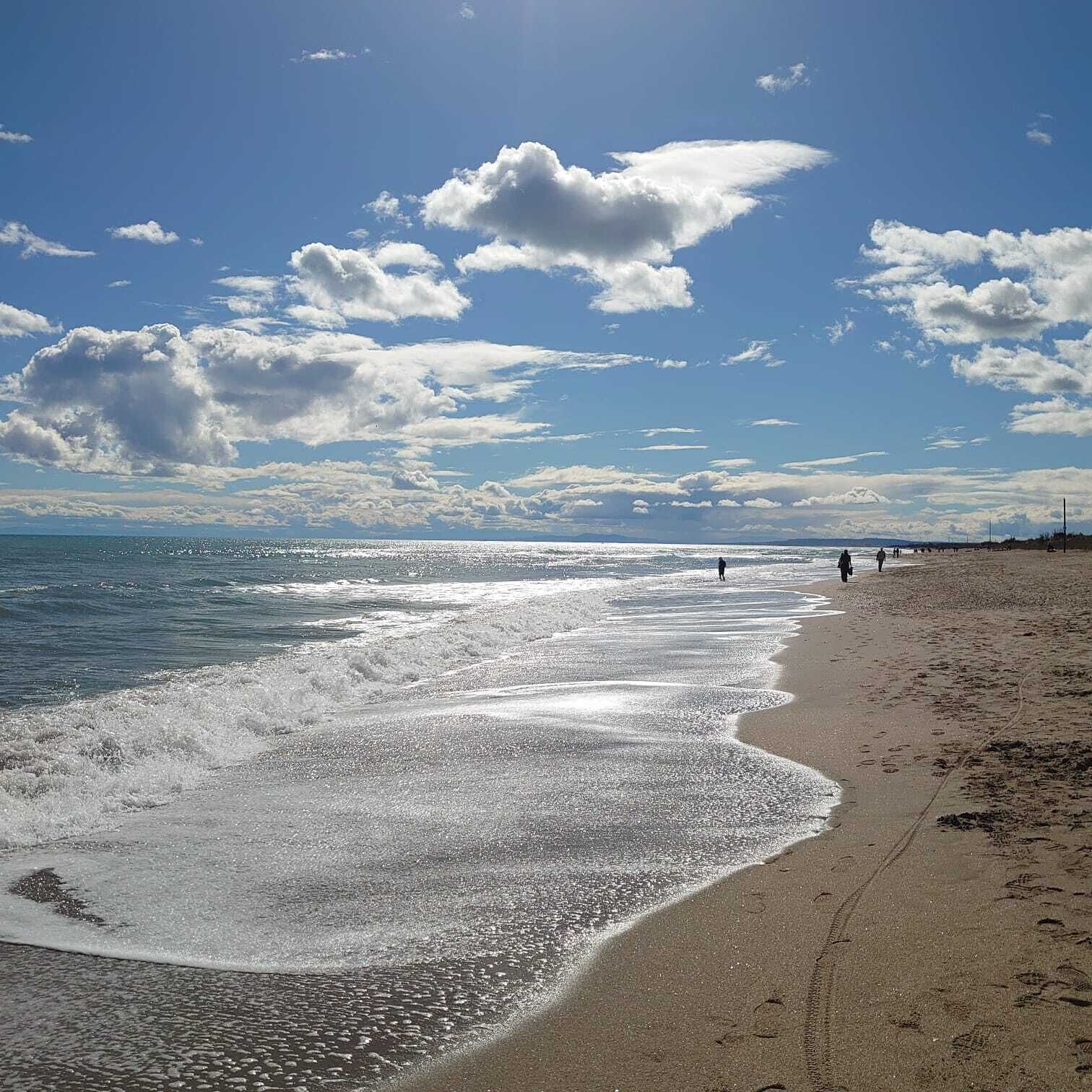 Een strand met een brede zandvlakte, rustige golven en een heldere lucht met enkele wolken.