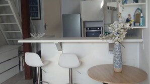 Une cuisine moderne avec un plan de travail blanc, trois tabourets de bar blancs, une table ronde en bois et un vase décoratif avec des fleurs.