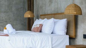 Uma cama com lençóis brancos, uma cabeceira de madeira e duas luminárias pendentes feitas de fibra.