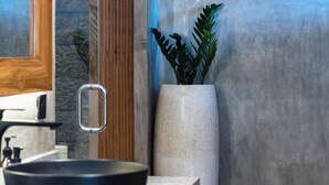 Um banheiro com pia moderna, um espelho grande e um vaso alto com uma planta.