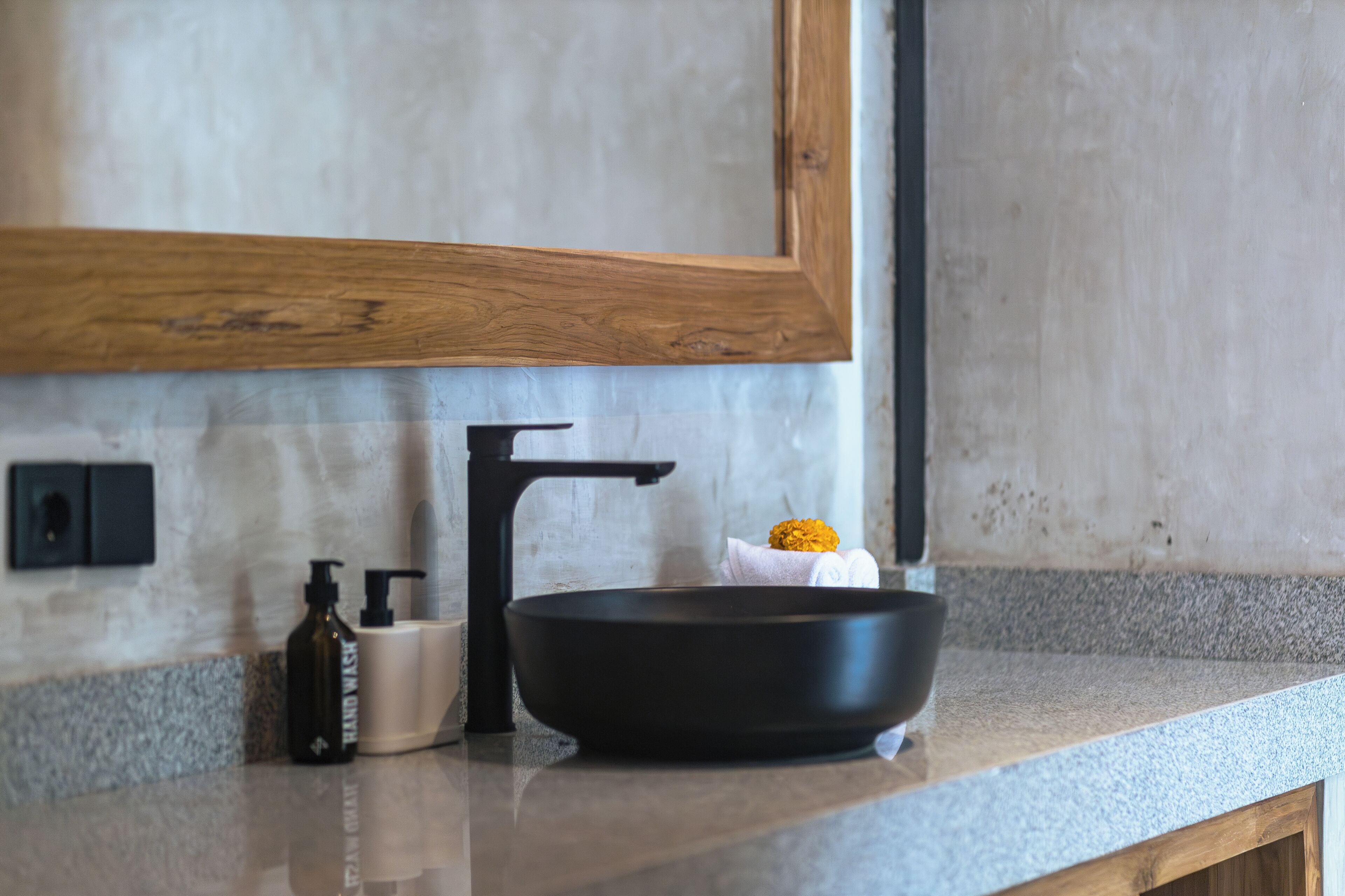 A modern kitchen with a black basin, a wooden frame above the sink, and a marble countertop.