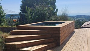 Ein hölzernes Whirlpool mit Stufen, umgeben von einer Holzterrasse und einer Rasenfläche.