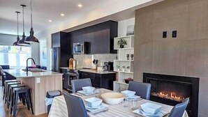 A modern kitchen with dark cabinetry, a central island, and a dining area with a fireplace.