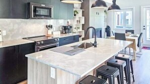 A modern kitchen with dark cabinetry, a central island with stools, a microwave, and pendant lighting.