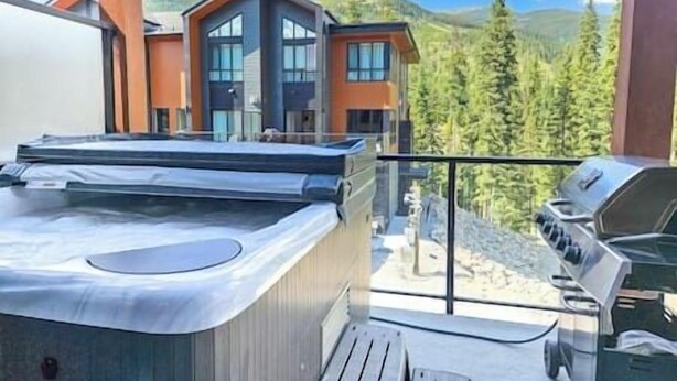 A hot tub on a balcony with a mountain view, a barbecue grill, and a wooden deck.