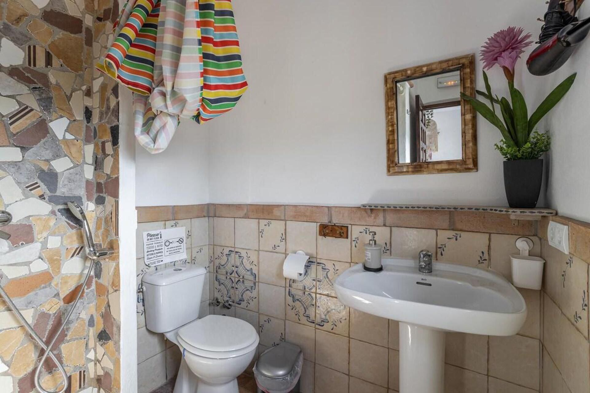 A bathroom with a mosaic tile wall, a white sink, a toilet, and a shower.