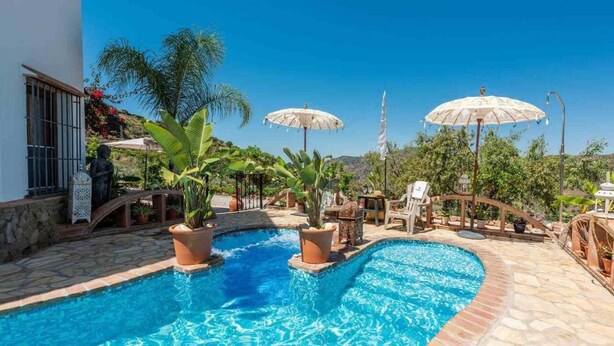 Un área de piscina con dos sombrillas, plantas en macetas y una estatua.