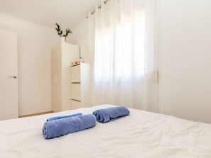 A hotel room with a bed, a wardrobe, and a window with sheer curtains.