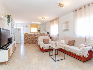 Ein Wohnzimmer mit Fernseher, Sofa, Couchtisch und einer Küche im Hintergrund.
