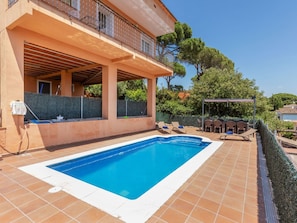 A swimming pool with a tiled deck, a covered patio area, and a view of surrounding greenery. - Panoramic by Interhome (Tordera)