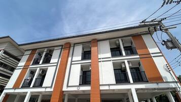 A multi-story building with a white facade and orange accents, featuring balconies and air conditioning units.