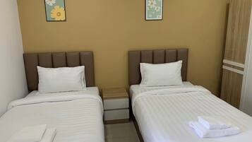 A hotel room with two beds, each with a pillow and a folded towel. There are two small flower paintings on the wall.