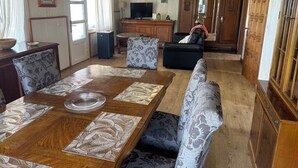 Uma sala de estar ampla com uma mesa de jantar de madeira, sofás estampados e uma televisão.