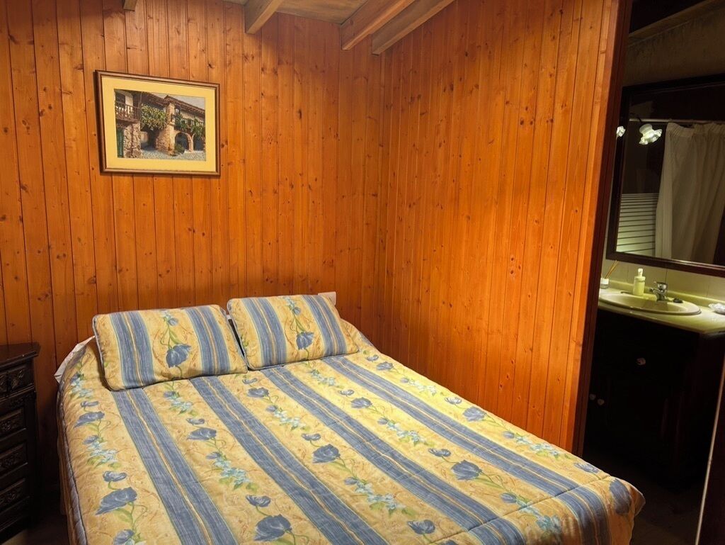 Un dormitorio con paneles de madera, una cama con ropa de cama floral, un aparador y un baño con lavamanos y espejo.