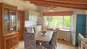 Cozinha com armários de madeira, mesa de jantar com cadeiras estampadas, geladeira e janela com vista para vegetação.