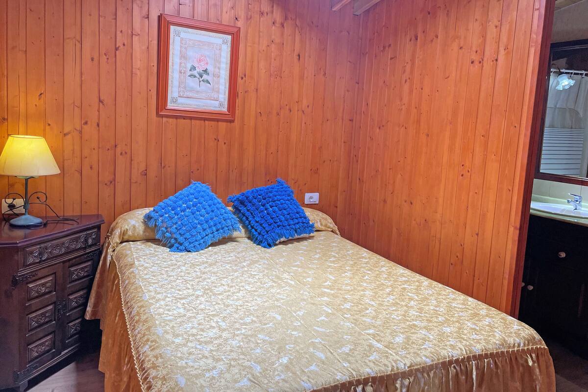 Una stanza con rivestimento in legno, un letto, un comodino con una lampada e un quadro appeso al muro.