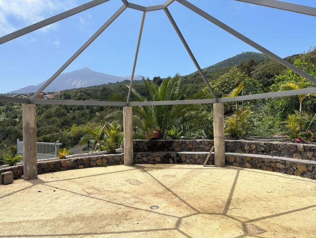 A covered outdoor area with a hexagonal floor plan, stone walls, and a view of a mountain.