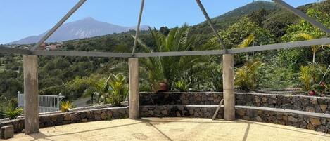A covered outdoor area with a hexagonal floor plan, stone walls, and a view of a mountain.