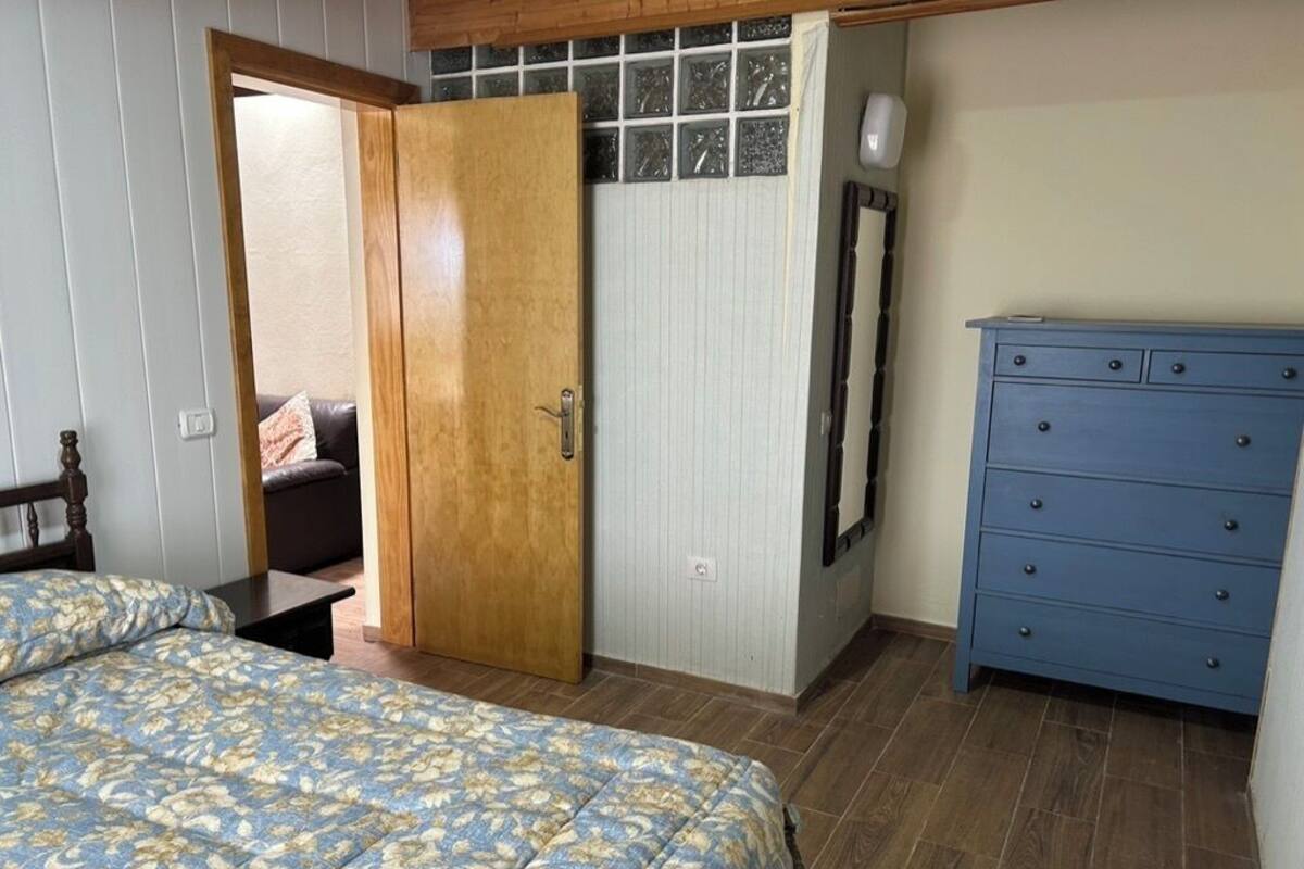 Una camera da letto con un letto, un armadio in legno, una cassettiera blu e una porta che dà su un'altra stanza.