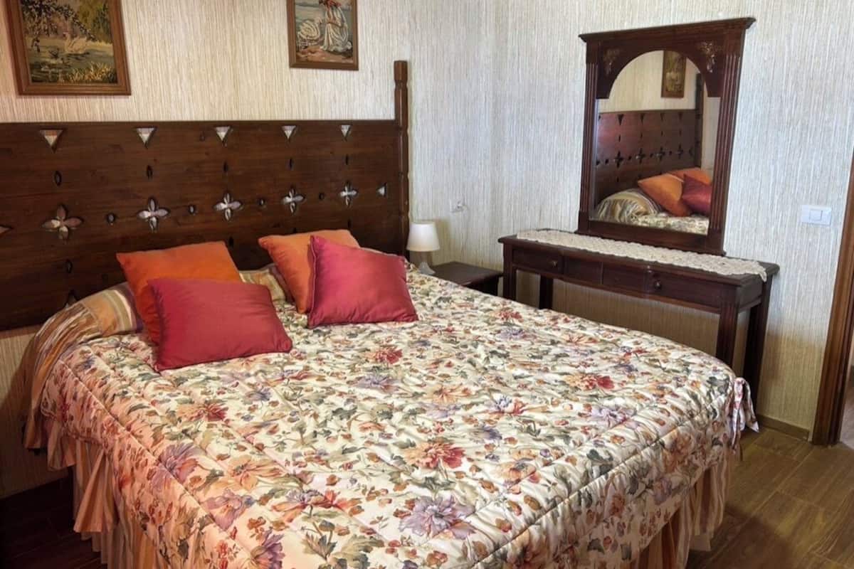 Una camera da letto con testiera in legno, copripiumino floreale e uno specchio sopra il comò.