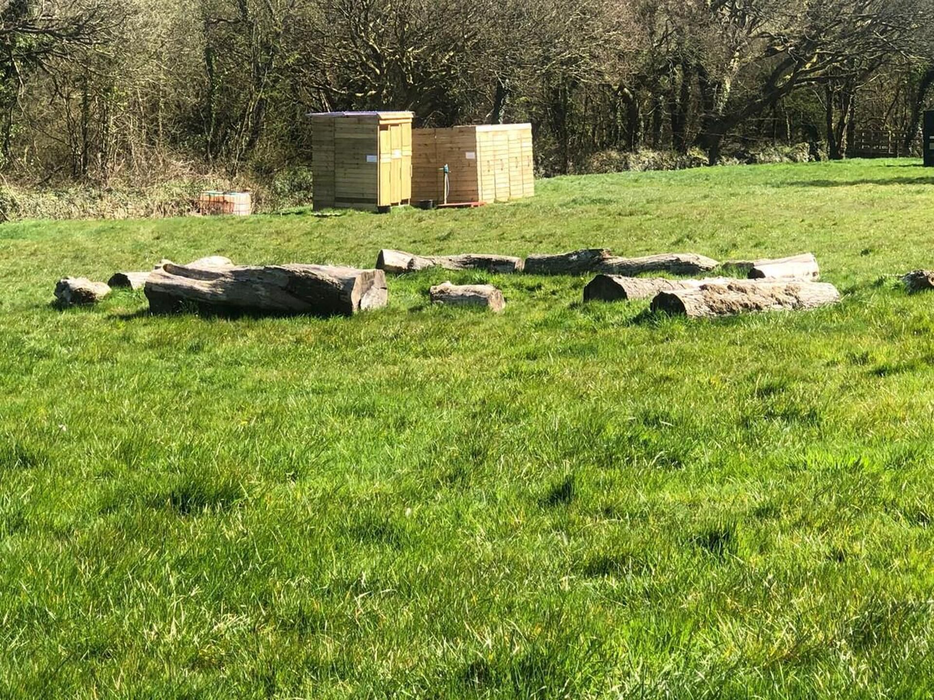 A wooden structure in a grassy field with trees in the background.