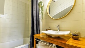 Une salle de bain avec un lavabo blanc, un meuble-lavabo en bois, un miroir avec un cadre doré et un espace douche.
