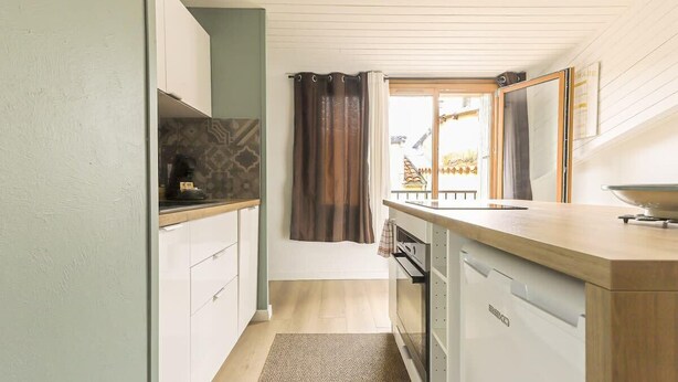 Une cuisine compacte avec des meubles blancs, un plan de travail en bois et un lave-vaisselle encastré.