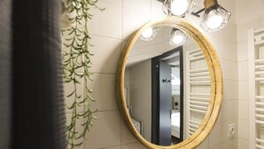Une salle de bain avec un miroir rond, un porte-serviettes et une plante suspendue.