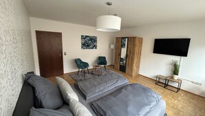 Ein modernes Hotelzimmer mit einem großen Bett, einer Sitzecke, zwei Sesseln, einem kleinen Tisch, einem Fernseher und einem Spiegel.