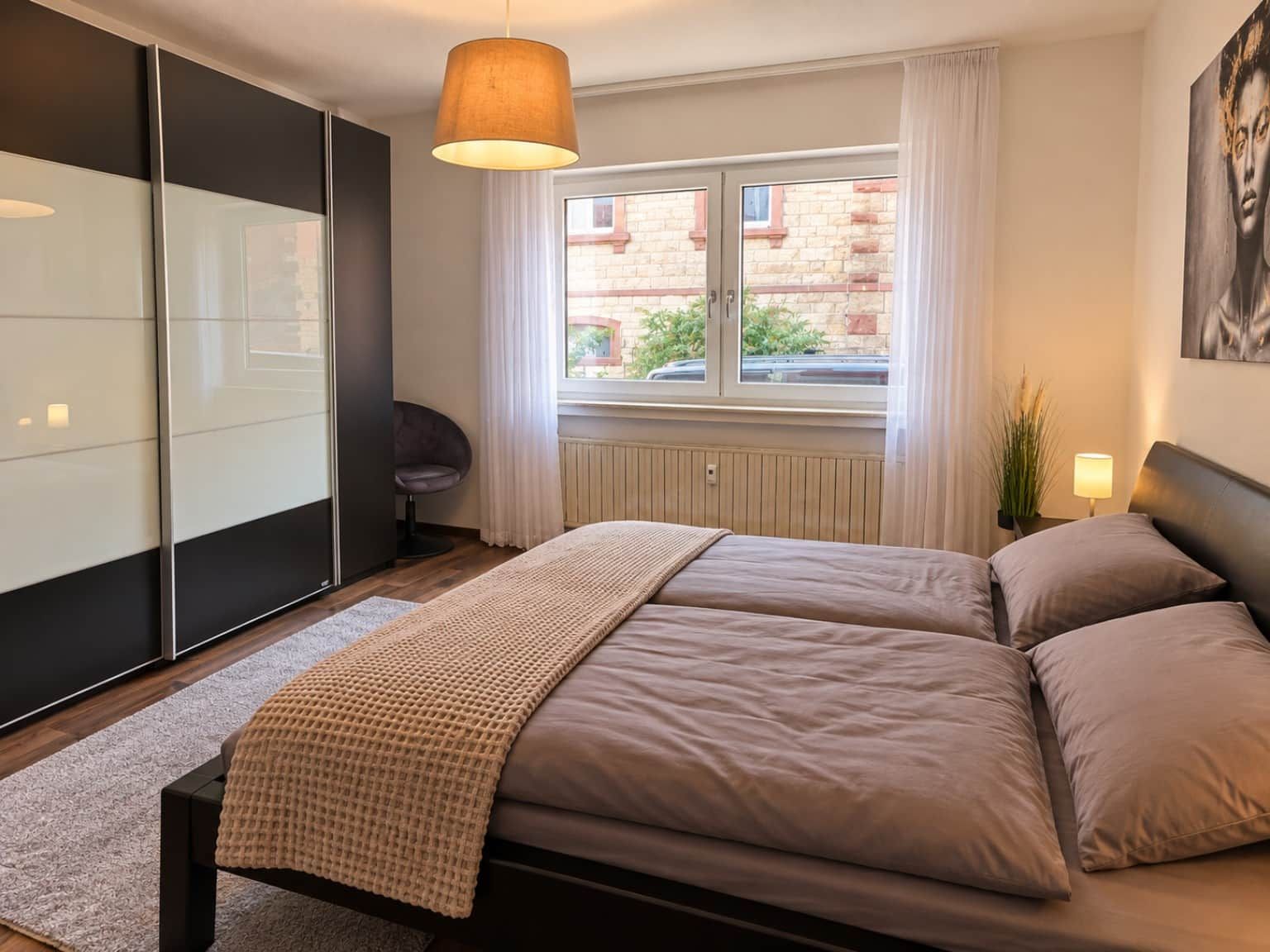 A modern bedroom with a bed, a chair, a window with curtains, and a painting on the wall.