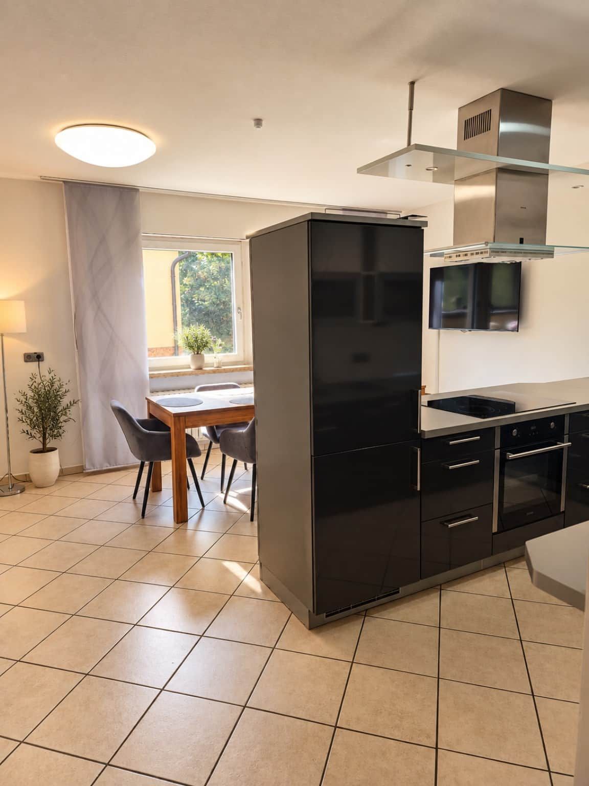 A modern kitchen with a black refrigerator, stainless steel appliances, and a dining area with a table and chairs.