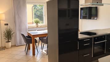 A modern kitchen with a black refrigerator, stainless steel appliances, and a dining area with a table and chairs.