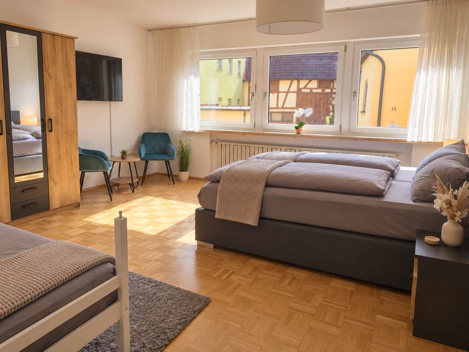 A bedroom with a bed, a chair, a desk, a radiator, and a window with curtains.