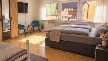 A bedroom with a bed, a chair, a desk, a radiator, and a window with curtains.