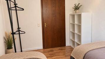 A room with two beds, a wooden door, a white shelving unit, and a black metal rack.