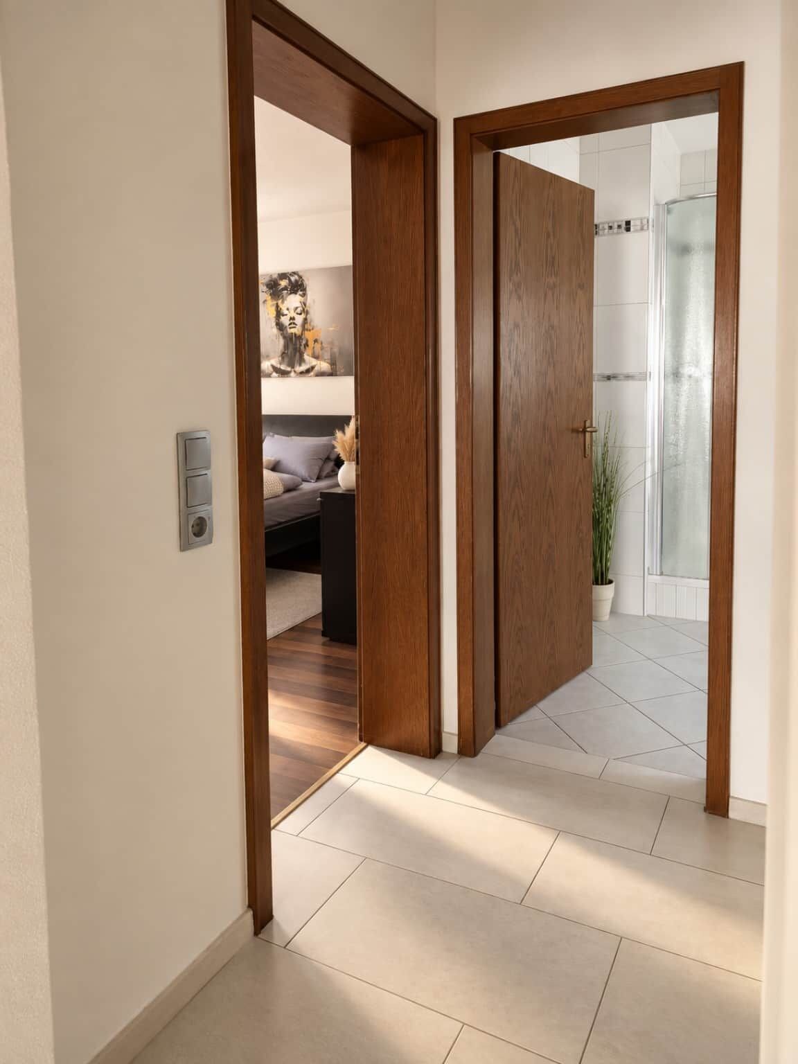 A hallway with a wooden door leading to a bathroom with a glass shower.