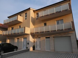A multi-story residential building with balconies, a garage, and a patterned driveway.